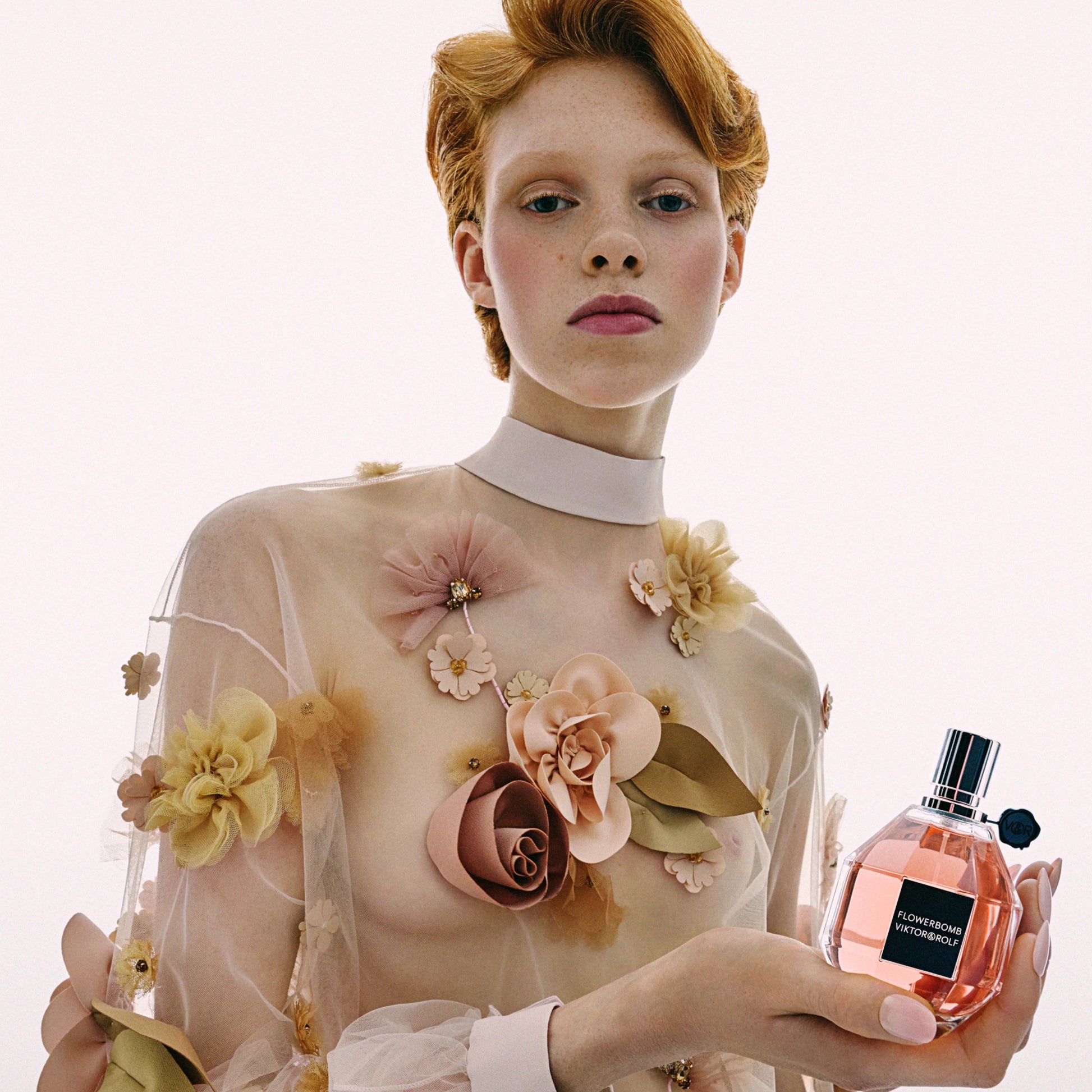 Woman holding a perfume bottle with floral dress against a white background