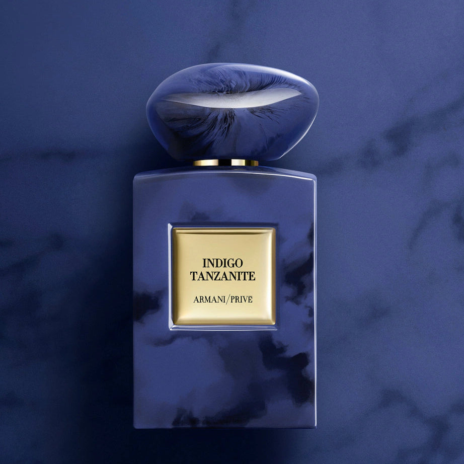 Armani Privé Indigo Tanzante perfume bottle with a dark blue marbled body and cap, featuring a gold label, set against a dark blue marble background.