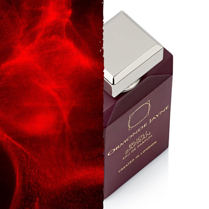 A perfume bottle labeled 'Orchidize by Jane' in deep burgundy with a silver cap, shown on a white background next to a textured red smoke graphic.