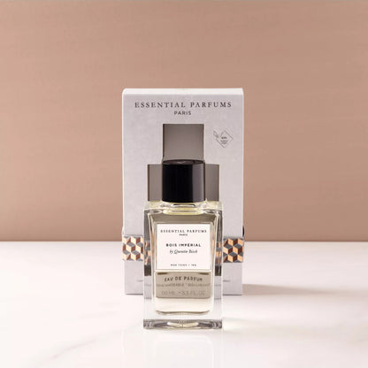 A bottle of Essential Parfums Paris 'Le Bonheur' Eau de Parfum with its white packaging box, displayed on a white marble surface against a warm beige background.