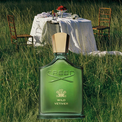 Creed Wild Vetiver perfume bottle in a grassy outdoor setting with a table and chairs.