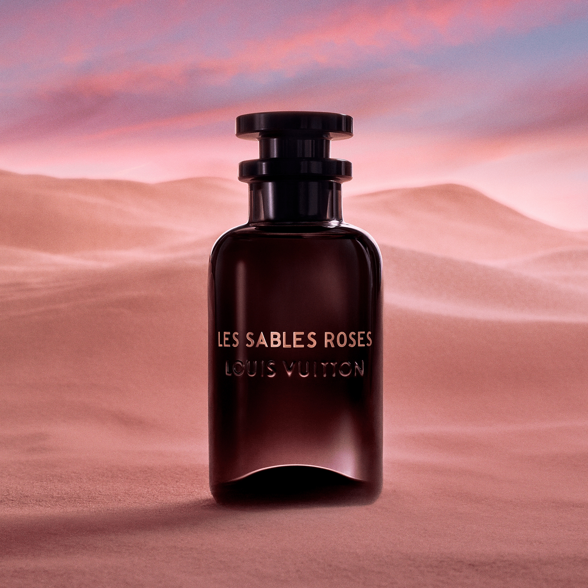 Louis Vuitton Les Sables Roses perfume bottle against a desert sunset background