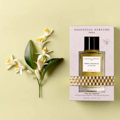 A bottle of Essential Parfums Paris Vergi-Botanica Eau de Parfum next to its packaging box, styled with white flowers and green leaves on a pale yellow-green background.