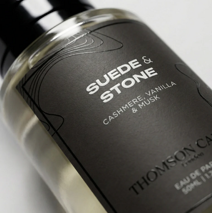 Thomson Carter & Scents 'Suede & Stone' Eau de Parfum bottle, featuring a matte black label with white text and a clear glass bottle showing the light-colored liquid inside.