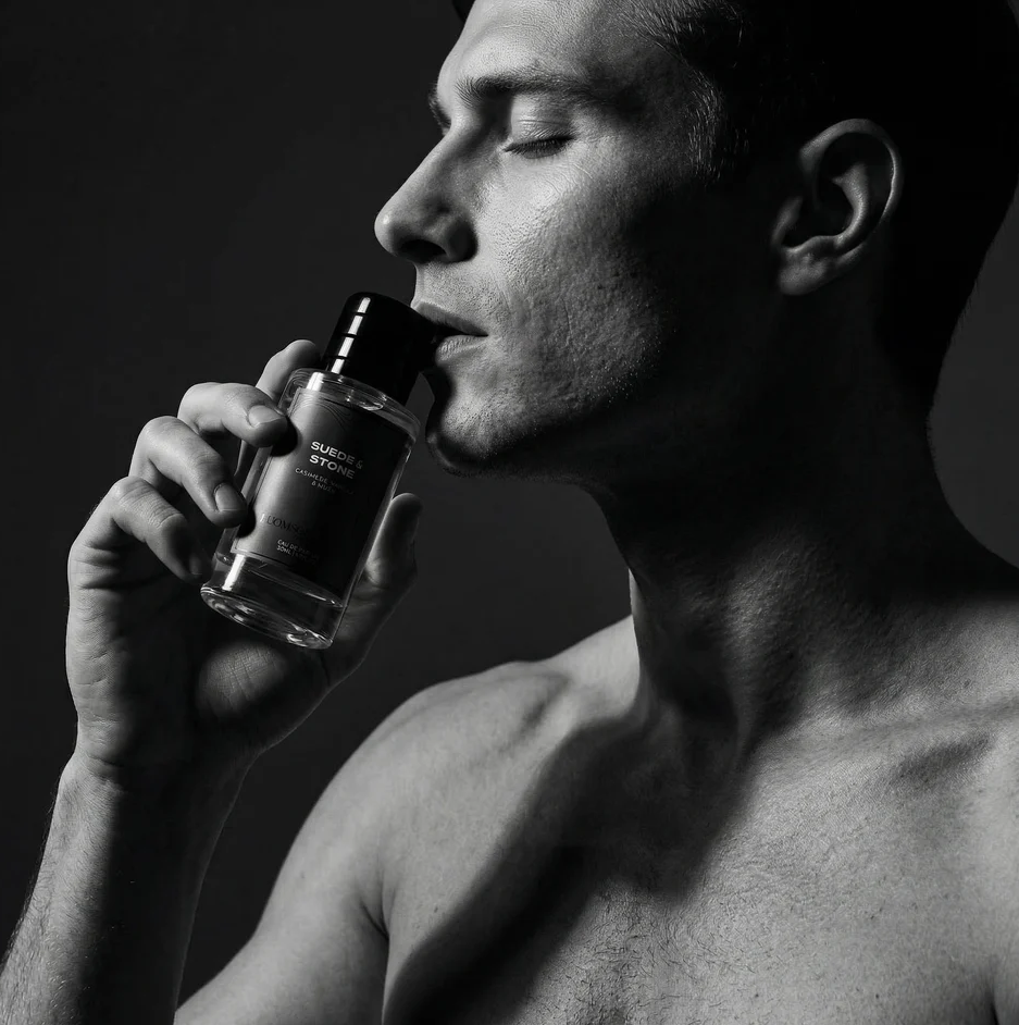 Man holding a perfume bottle of thomson carter suede and stone with a dark background