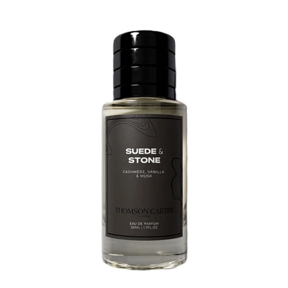 A bottle of Thomson Carter Suede & Stone Eau de Parfum, featuring a clear glass bottle with a black cap and a dark charcoal label with white text.