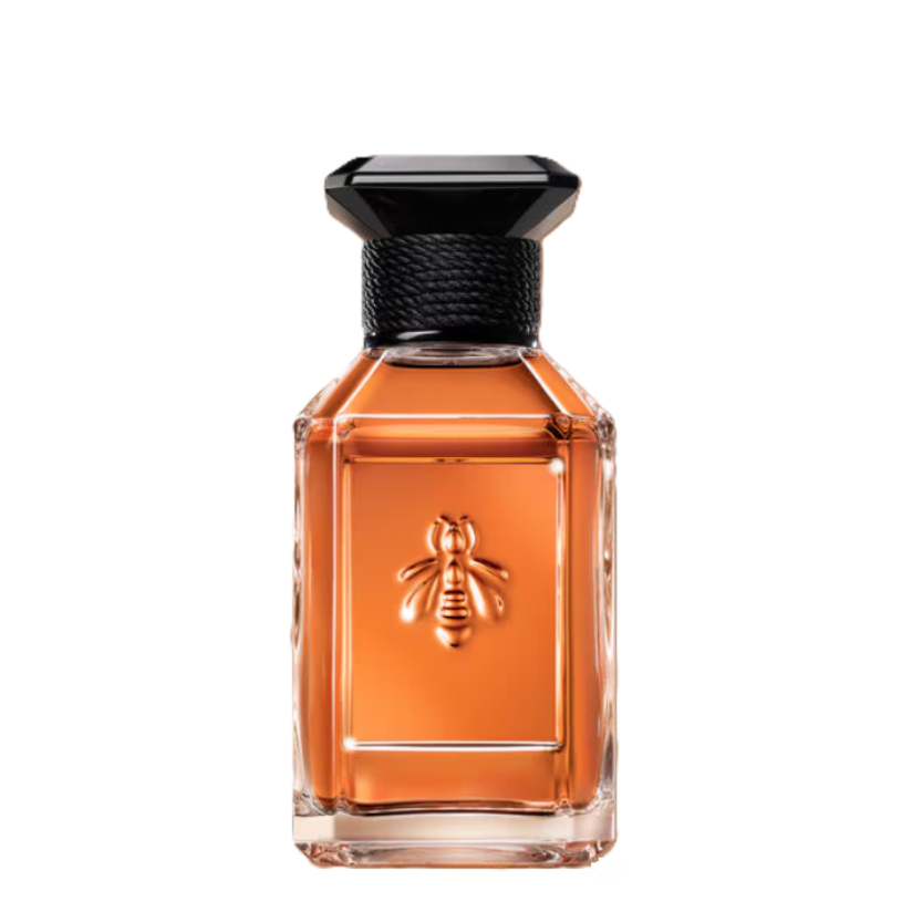 A rectangular glass perfume bottle filled with amber-orange liquid, featuring an embossed bee on the front and a black faceted cap, isolated on a white background.