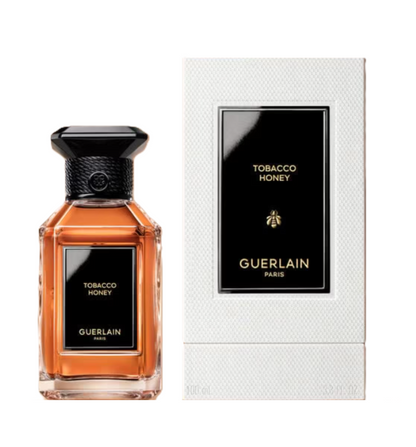 Guerlain Tobacco Honey perfume bottle next to its white textured packaging box, featuring a black label with gold lettering.