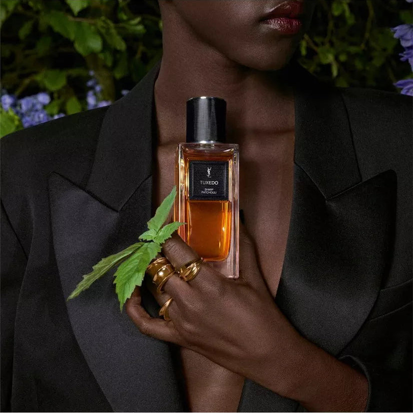 Person holding a perfume bottle with a plant, against a blurred natural background